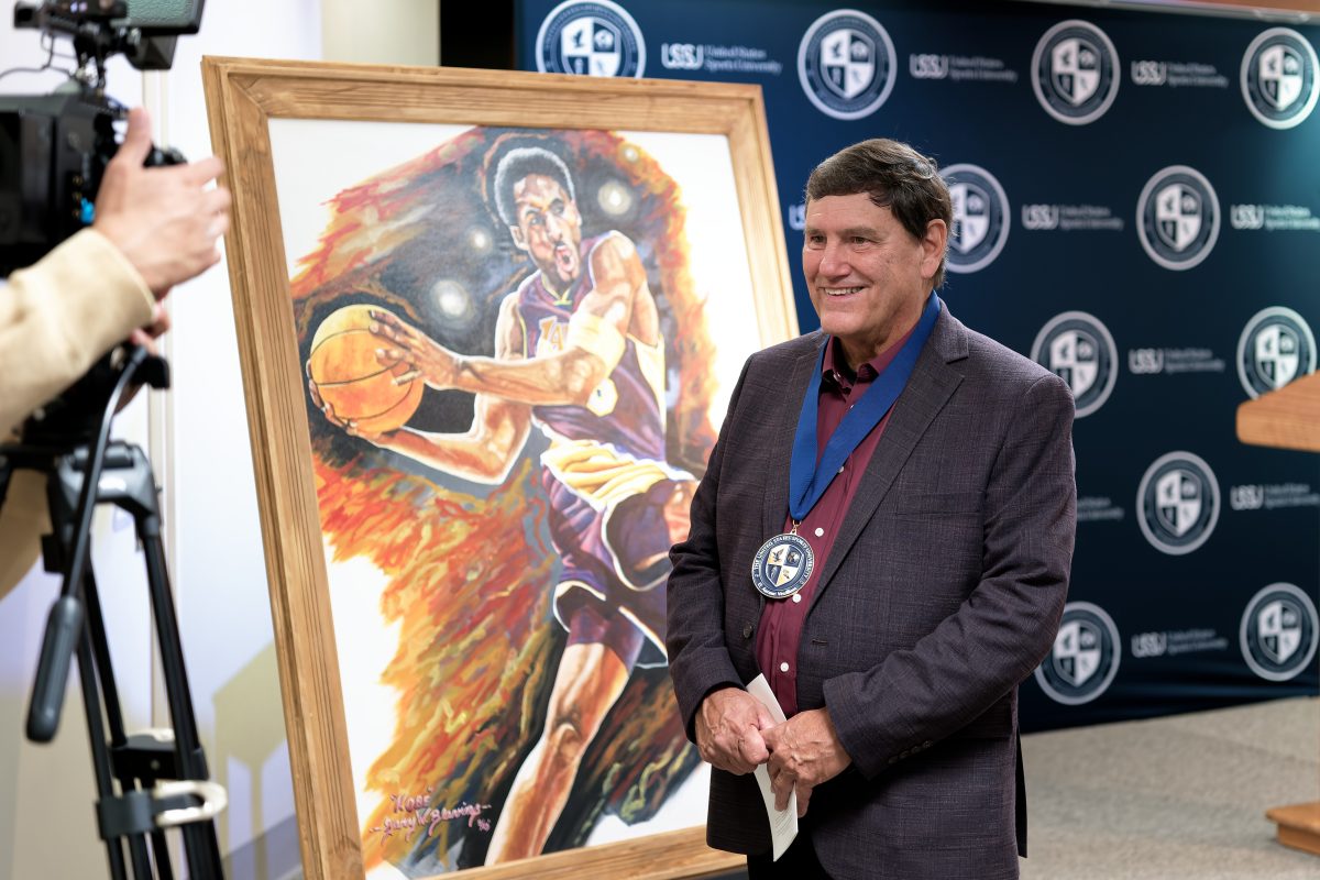 A medallion recipient beside a basketball painting at the Sport Artist of the Year celebration.